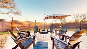 Un patio con sillas Adirondack, un pozo de fuego y una sombrilla.