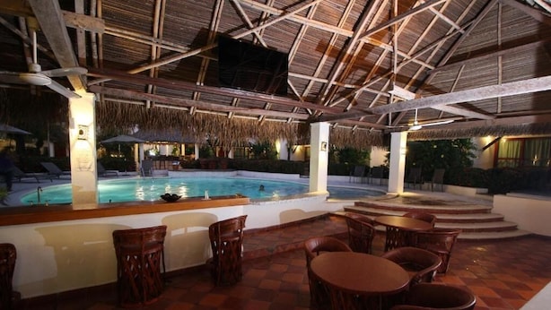 An indoor pool area with a thatched roof, surrounded by wooden chairs and tables. - HOTEL VILLA BLANCA SUITES (San Juan Bautista Tuxtepec)