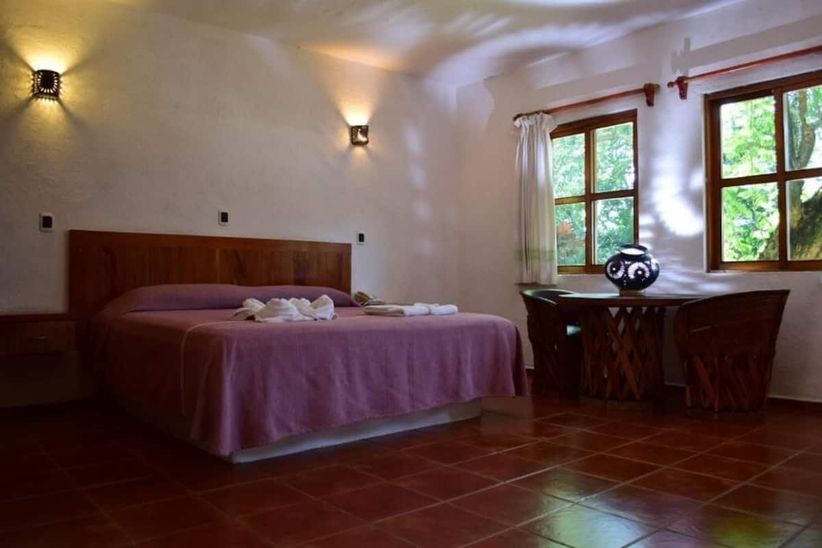 A bedroom with a wooden bed, a desk with a chair, and a window with curtains.
