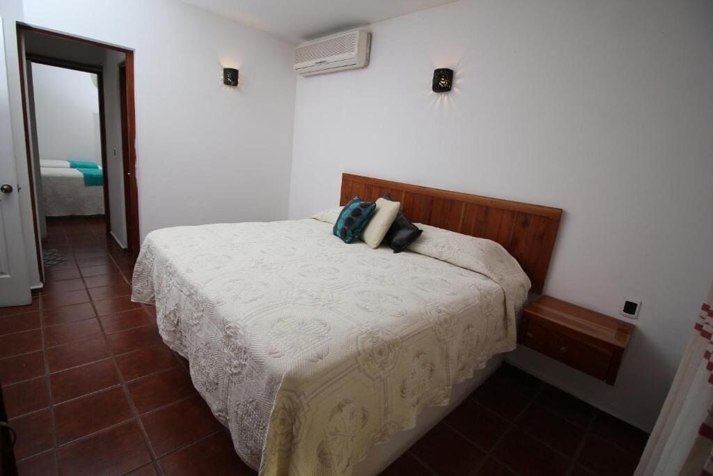 A bedroom with a bed, a nightstand, an air conditioning unit, and a door leading to another room.