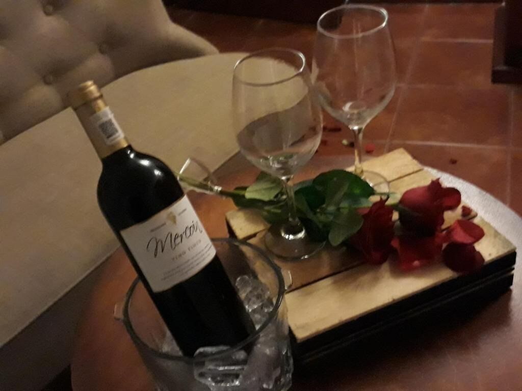 Una botella de vino, dos copas y una caja con pétalos de rosa sobre una mesa de madera.