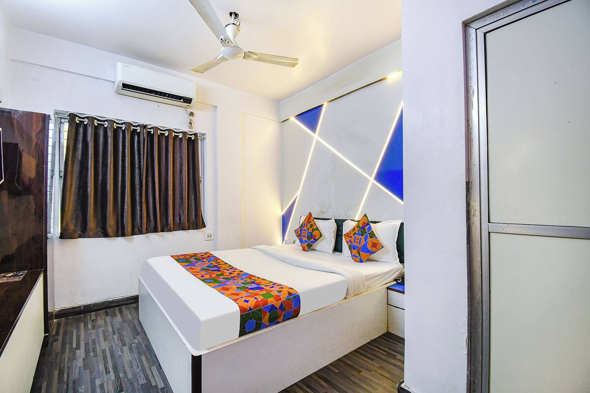 Ein kleines Hotelzimmer mit Bett, Deckenventilator, Klimaanlage und einem Fenster mit Vorhängen.