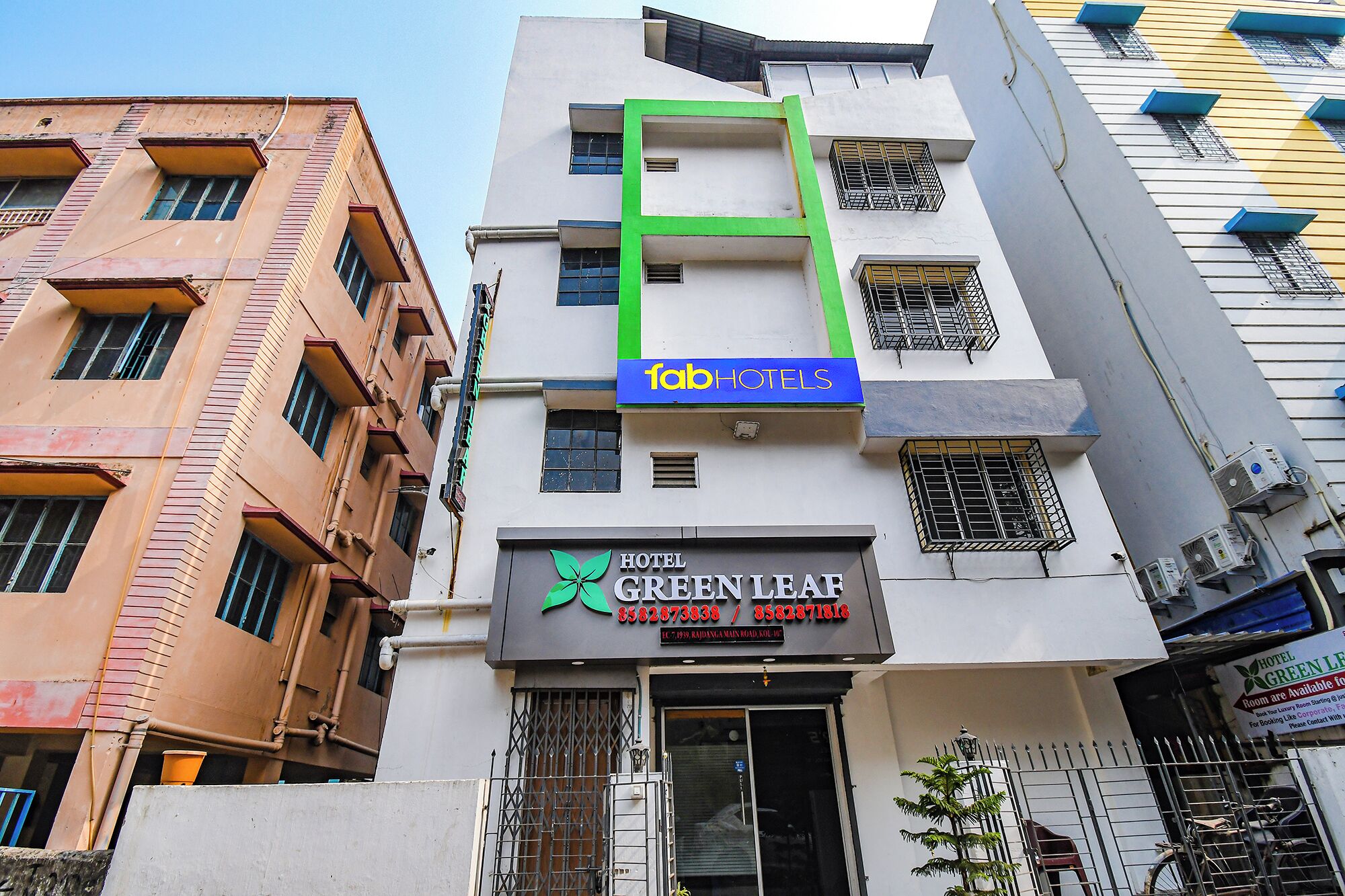 A hotel named 'Hotel Green Leaf' with a modern facade, a prominent green vertical feature, and a sign for 'Fab Hotels'.