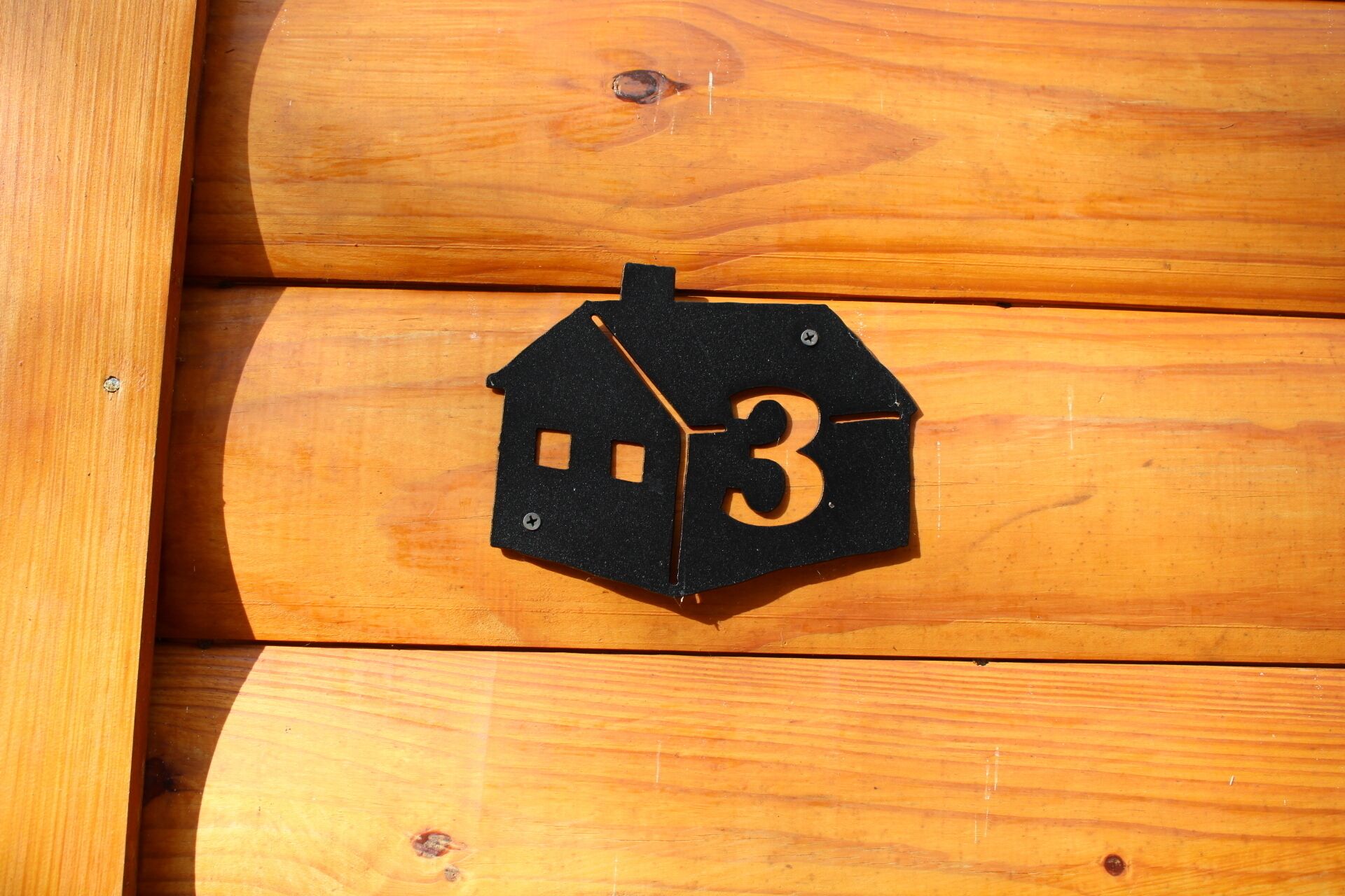 A black house-shaped sign with the number 3 on a wooden surface.