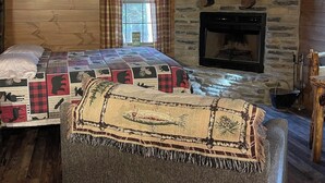 Una habitación tipo cabaña acogedora, con cama, televisión instalada en una pared de piedra y chimenea.