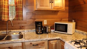 Una cocina con armarios de madera, encimera de granito, pileta, cafetera, tostadora, horno microondas y cocina a gas.