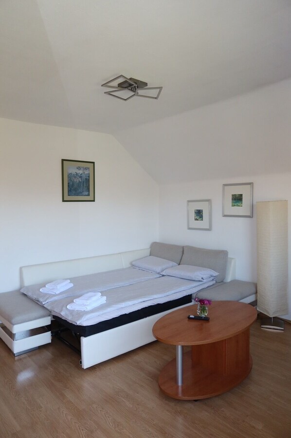 Ein modernes, minimalistisches Schlafzimmer mit Bett, Sofa, rundem Holztisch und Deckenventilator.
