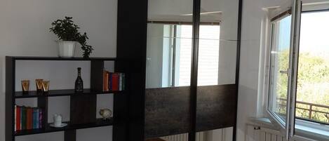 Een slaapkamer met een bed, een boekenkast, een spiegel en een raam.