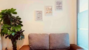 A grey sofa with a brown throw blanket, a large green plant, and three framed inspirational quotes on the wall. - “Modern Cozy Unit with Balcony & Fast Wi-Fi – Near SM Bicutan” (Parañaque)