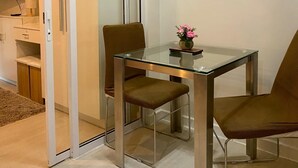 A modern dining area with a glass table and metal chairs, a sliding door leading to a kitchen, and a flat-screen TV mounted on the wall. - “Modern Cozy Unit with Balcony & Fast Wi-Fi – Near SM Bicutan” (Parañaque)