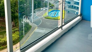 A modern hotel room with large windows offering a view of a busy intersection and a multi-story building. - “Modern Cozy Unit with Balcony & Fast Wi-Fi – Near SM Bicutan” (Parañaque)