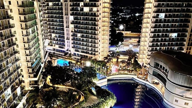 A high-rise hotel with multiple balconies, a central swimming pool, and a sunken bar area. - “Modern Cozy Unit with Balcony & Fast Wi-Fi – Near SM Bicutan” (Parañaque)