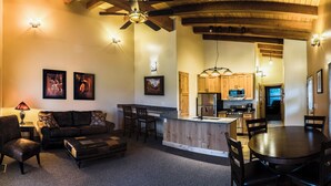 A cozy living room with a sofa, ottoman, and a dining area with a table and chairs. There is a kitchen with wooden cabinets and a central island. - Boulder Mountain Lodge (Boulder)