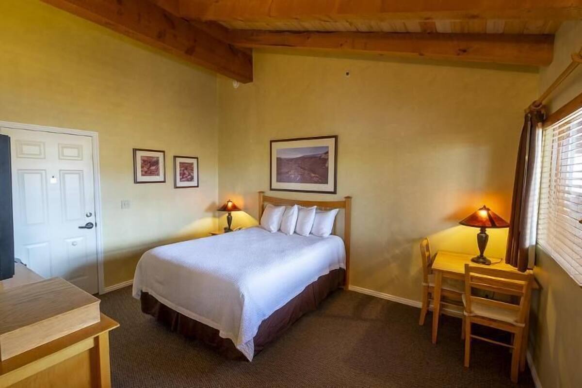 A bedroom with a bed, two bedside lamps, a desk, and a chair.