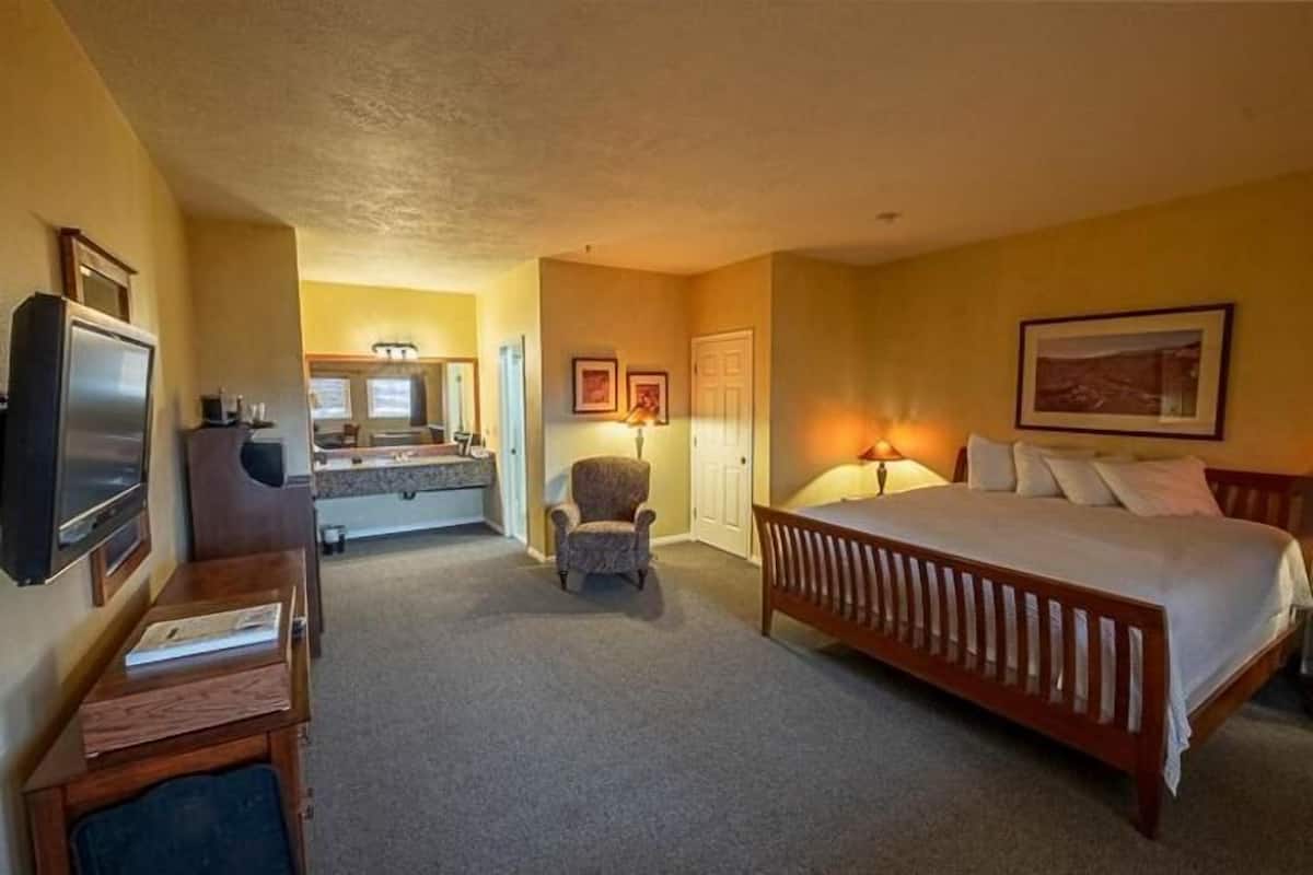 A hotel room with a bed, a desk, a chair, a television, and a bathroom visible in the background.