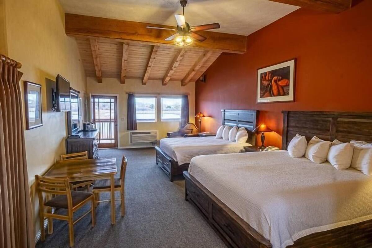 A hotel room with two beds, a desk, a chair, and a ceiling fan.