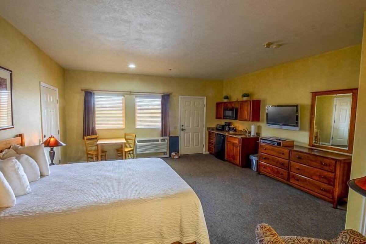 A hotel room with a large bed, a desk, a chair, a dresser, a television, and a window with blinds.
