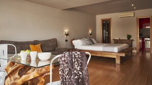 Een moderne slaapkamer met een glazen eettafel, een houten bed en een kitchenette op de achtergrond.