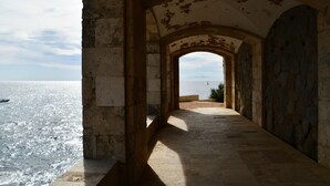 Ein gewölbter Gang mit Steinwänden, der zum Blick auf das Meer führt.