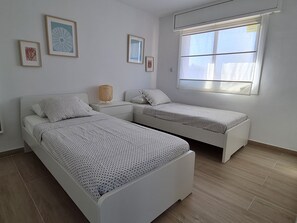 A modern bedroom with two single beds, a bedside table with a lamp, and a window with blinds. - Apartment in Ságaró with sea view and swimming pool (Sant Feliu de Guíxols)