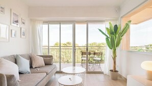 Ein modernes Wohnzimmer mit einer Couch, zwei kleinen runden Tischen, einer Topfpflanze und einem Balkon mit Gartenmöbeln.