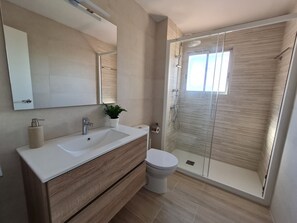 A modern bathroom with a white sink, wooden vanity, a toilet, and a glass-enclosed shower. - Apartment in Ságaró with sea view and swimming pool (Sant Feliu de Guíxols)