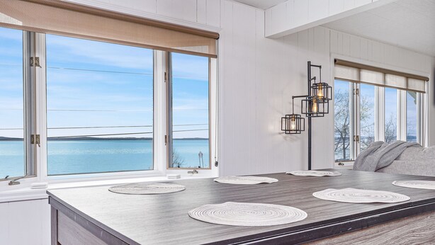A modern kitchen with a large island, large windows with a view of the water, and a built-in light fixture.