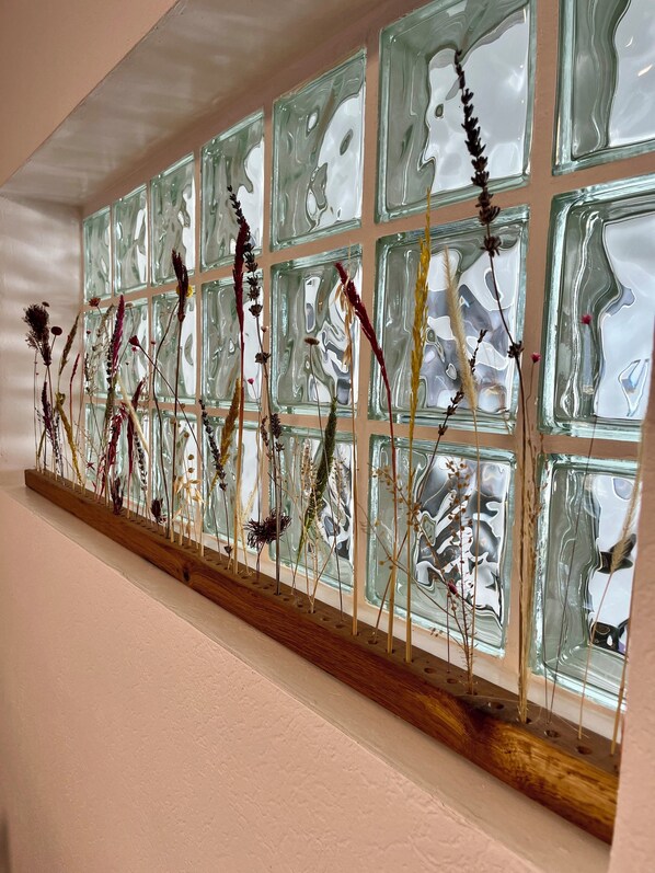 A wall with a series of square glass panels and a wooden shelf displaying dried plants.