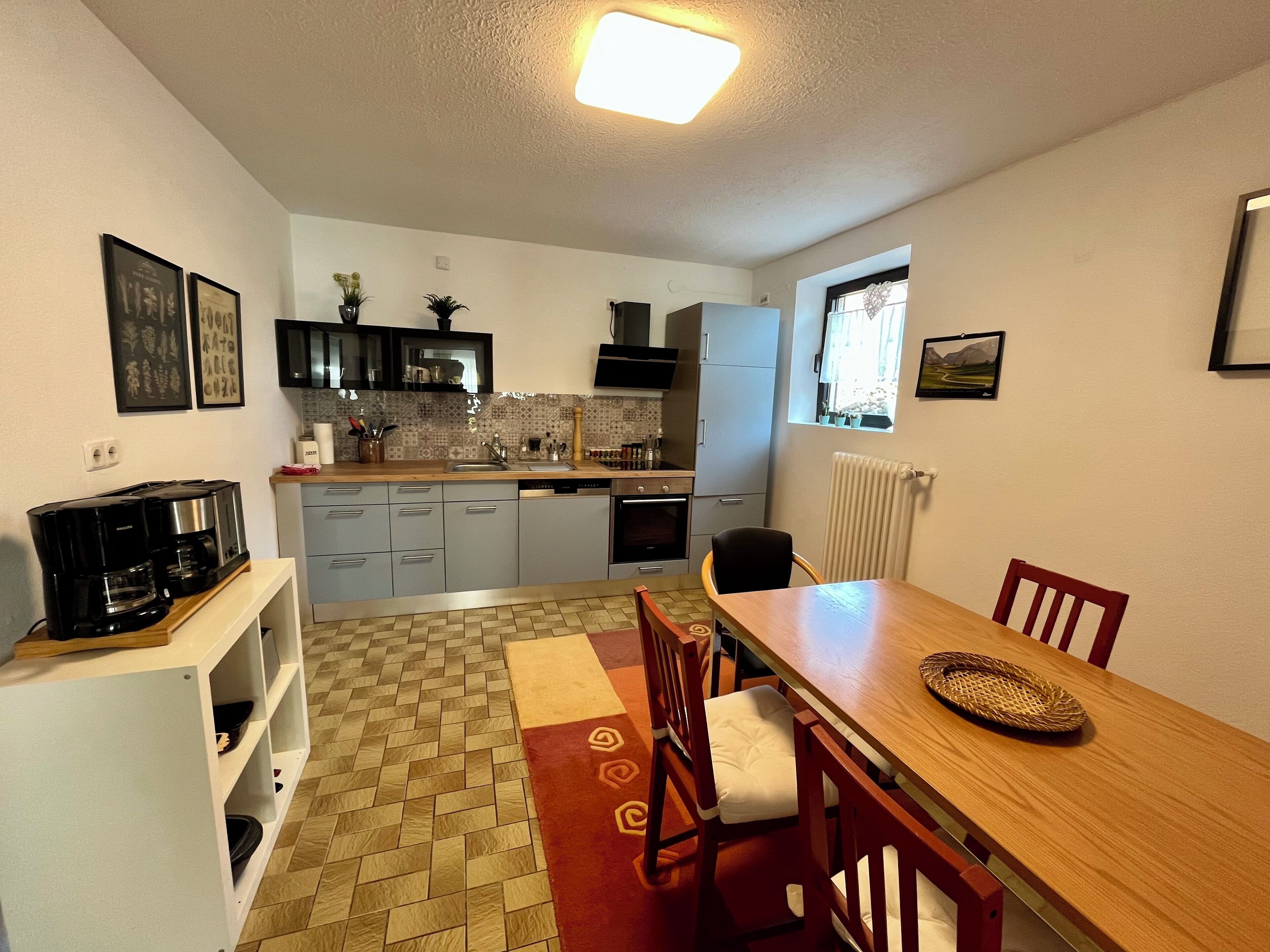 A compact kitchen with a dining area, featuring a coffee maker, cabinets, and a window with a view.