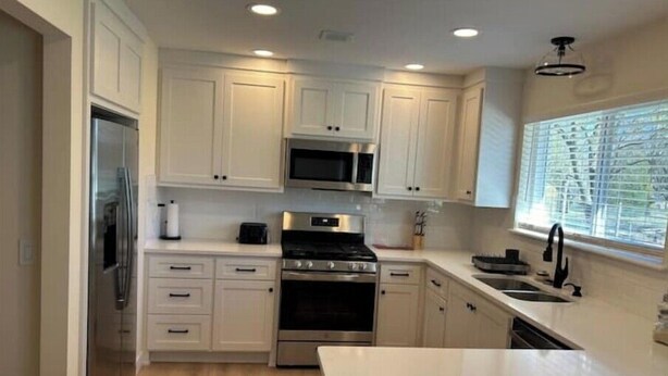 Una cocina moderna con armarios blancos, electrodomésticos de acero inoxidable y un amplio ventanal que proporciona luz natural.