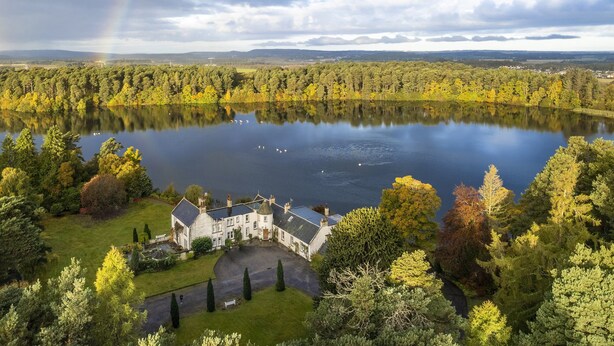 Una extensa propiedad con un lago, rodeada de un bosque frondoso y una casa señorial.