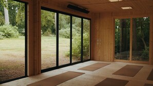 Una habitación con amplios ventanales, suelo de madera y colchonetas de yoga.