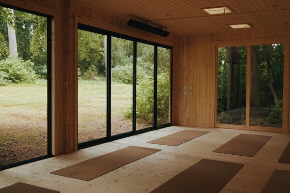 Una habitación con amplios ventanales, suelo de madera y colchonetas de yoga.