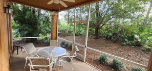 A covered patio with a table and chairs, surrounded by lush greenery and trees.
