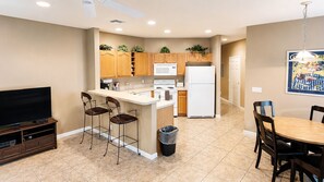 A modern kitchen with a central island, wooden cabinets, a microwave, a refrigerator, and a dining area with a table and chairs.