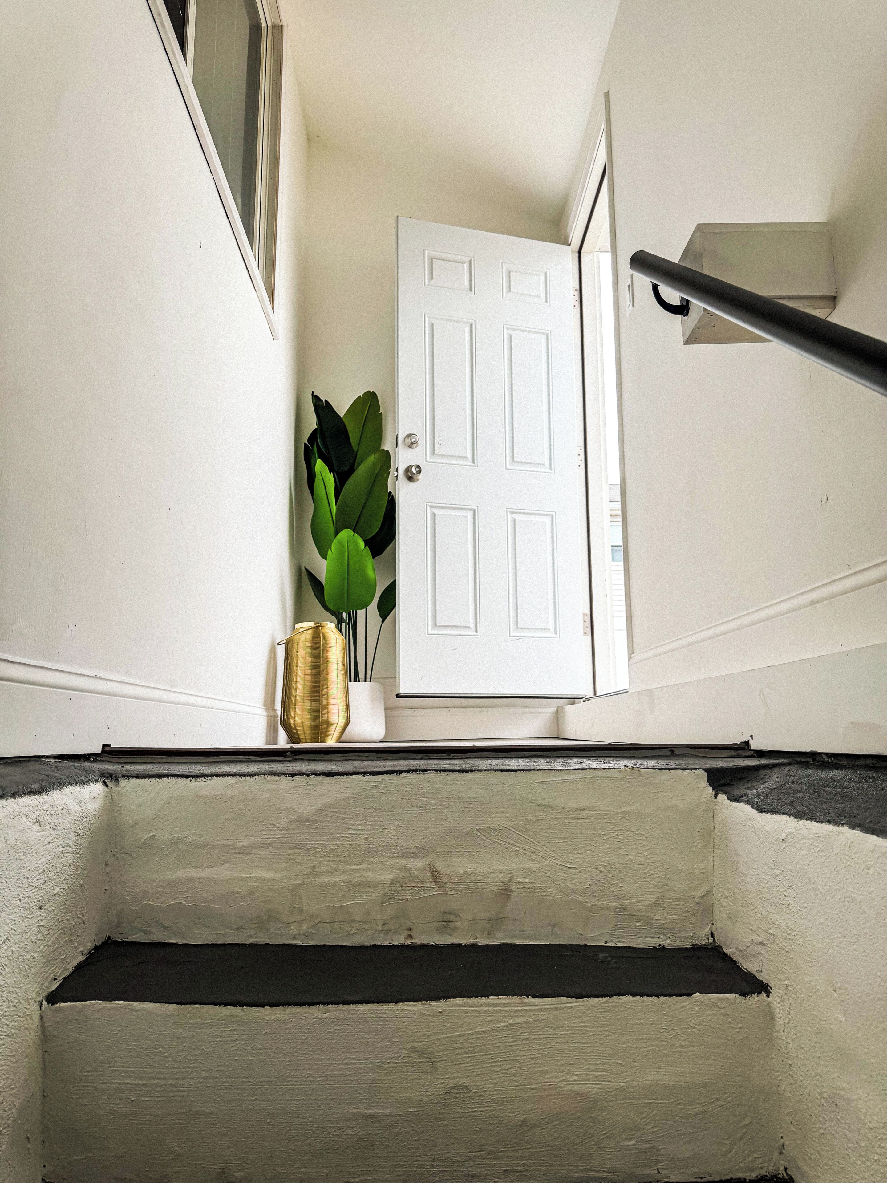 A white door with a handle, a small potted plant, and a gold-colored vase on a white wall.