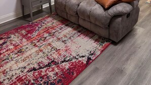 A grey sofa with a brown cushion, a small grey nightstand with a remote control, and a patterned rug on a wooden floor. - Lofts on Murphy by Rooms336 (Madison)