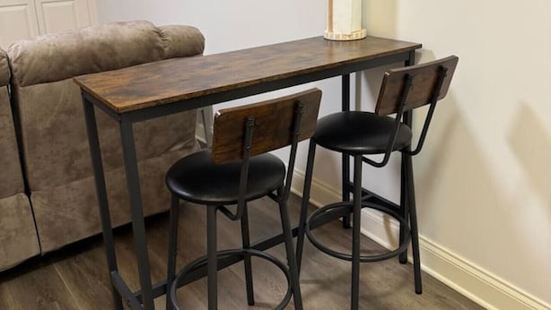 A small dining area with a wooden table and two black chairs. A beige sofa is against the wall, and a white door is visible. - Lofts on Murphy by Rooms336 (Madison)