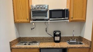 A compact kitchen with wooden cabinets, a built-in oven, a microwave, a sink, and a refrigerator. - Lofts on Murphy by Rooms336 (Madison)