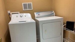 A laundry room with two stacked washers and dryers, a metal rack with a black item, and a vent on the wall. - Lofts on Murphy by Rooms336 (Madison)