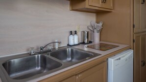Una cocina con dos fregaderos de acero inoxidable, armarios de madera, lavavajillas blanco y una encimera con utensilios de cocina y cafetera.