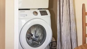 Un cuarto de lavandería con dos lavadoras apiladas y un tendedero.