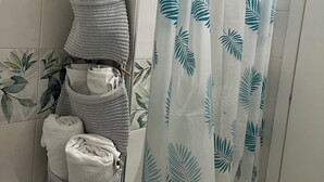 A bathroom with a towel rack holding several towels, a shower curtain with a leaf pattern, and a tiled wall with a leaf design. - Cottage frm home (Napoli)