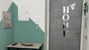 A room with a grey door marked "HOME" and a small table with a remote control. - Cottage frm home (Napoli)