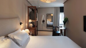 A hotel room with a bed, bedside lamps, a mirror, a small table with a vase, and a hanging coat rack. - Casa Teva Lisboa by chic&basic (Lisbon)