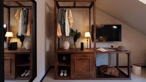 A modern hotel room with a wooden wardrobe, a mirror, a TV, a table with a lamp, a vase with a plant, and a pair of shoes. - Casa Teva Lisboa by chic&basic (Lisbon)