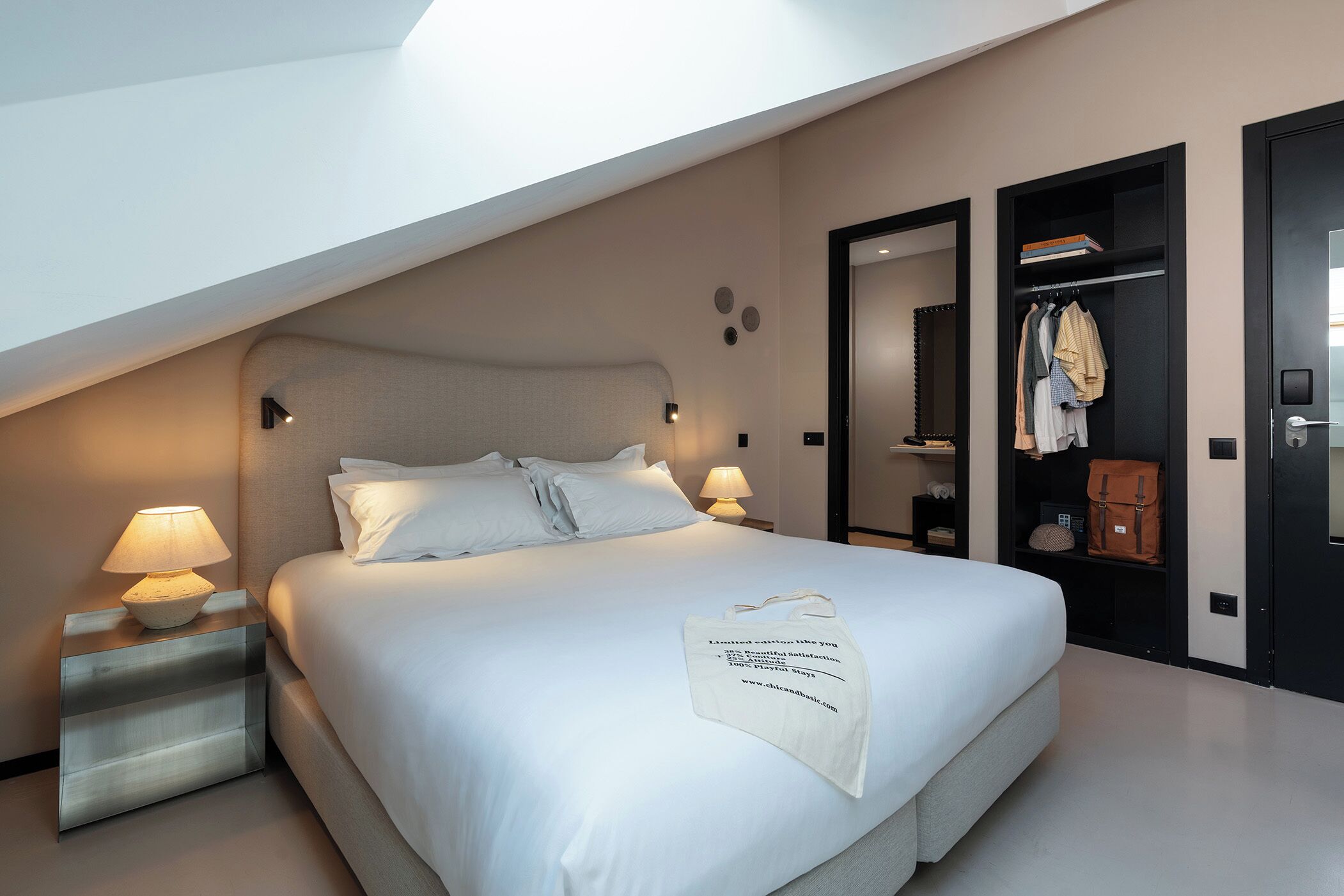 A modern bedroom with a bed, bedside lamps, a wardrobe, and a mirror.