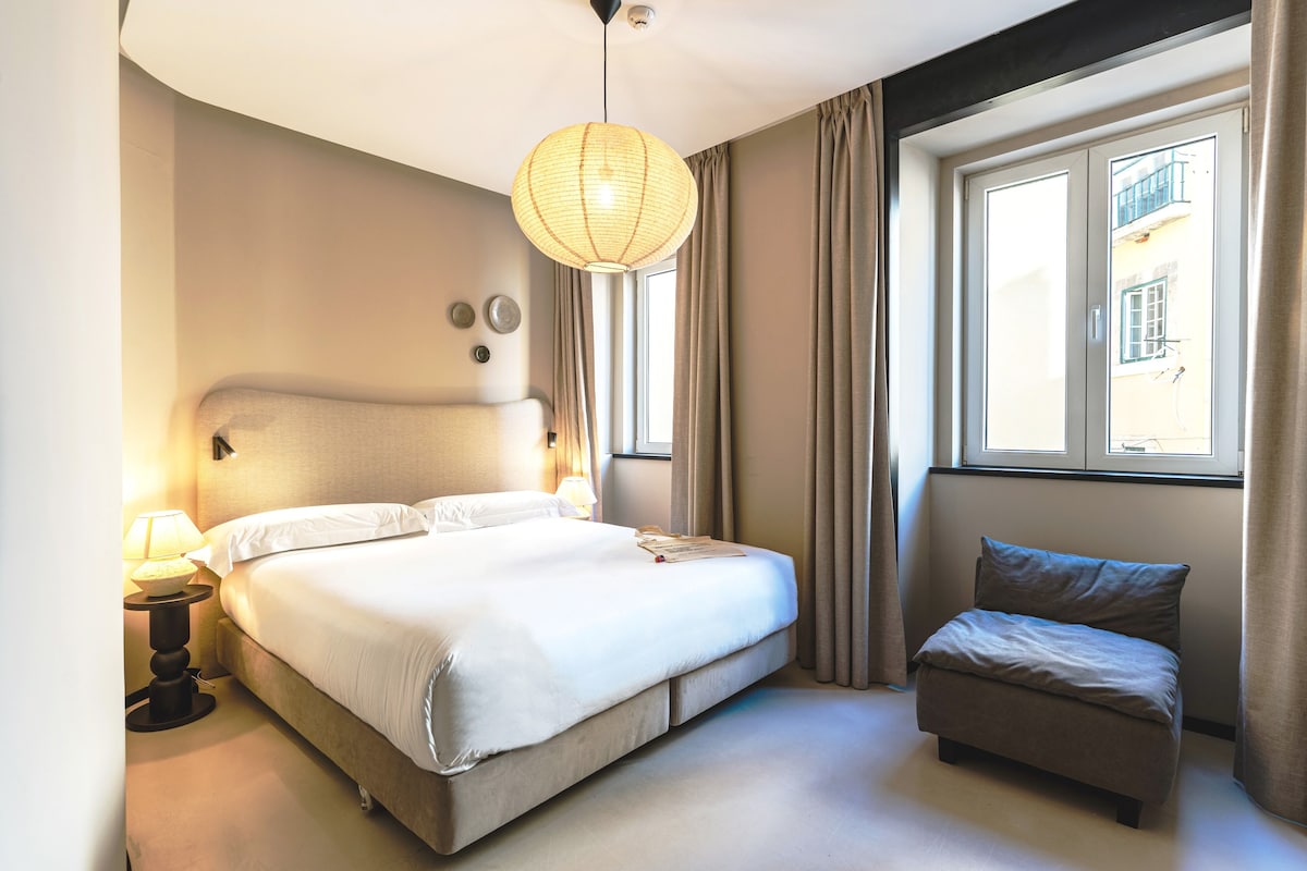 A hotel room with a bed, bedside lamp, and a window with curtains.