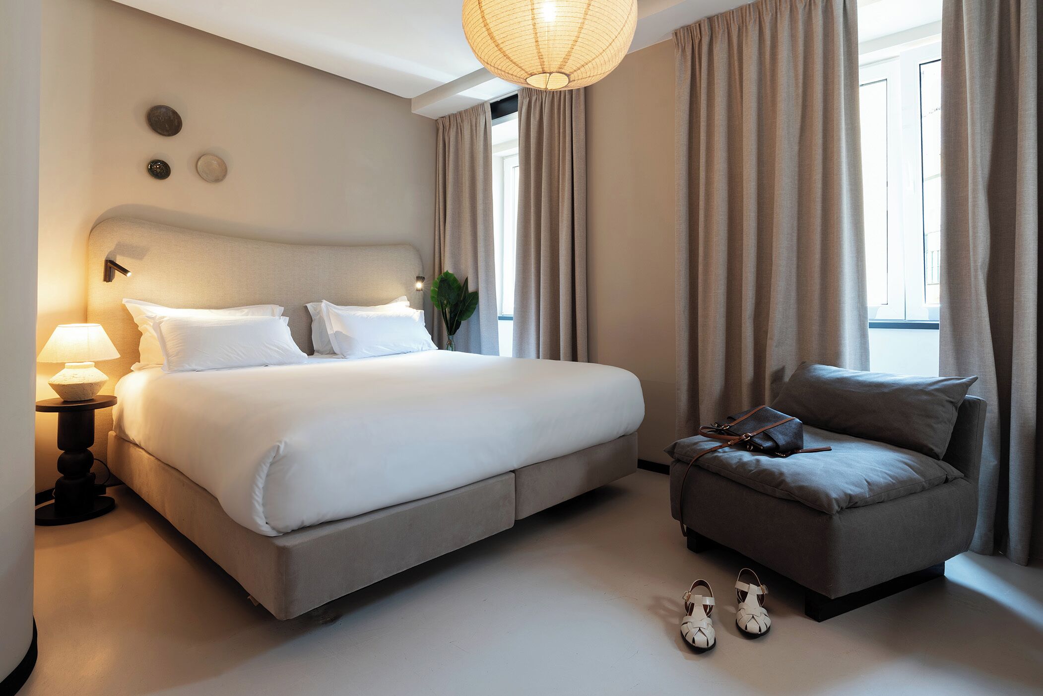 A modern hotel room with a large bed, a sofa, and a lamp.