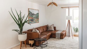 A modern living room with a brown leather sofa, a large potted plant, a wooden coffee table, and a painting on the wall. - Spacious Central Apartment (Stellenbosch)